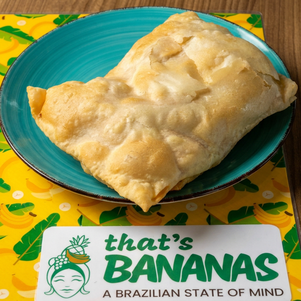 Golden baked pastry on a turquoise plate atop a banana-patterned tablecloth beside a That’s Bananas Brazilian restaurant card.